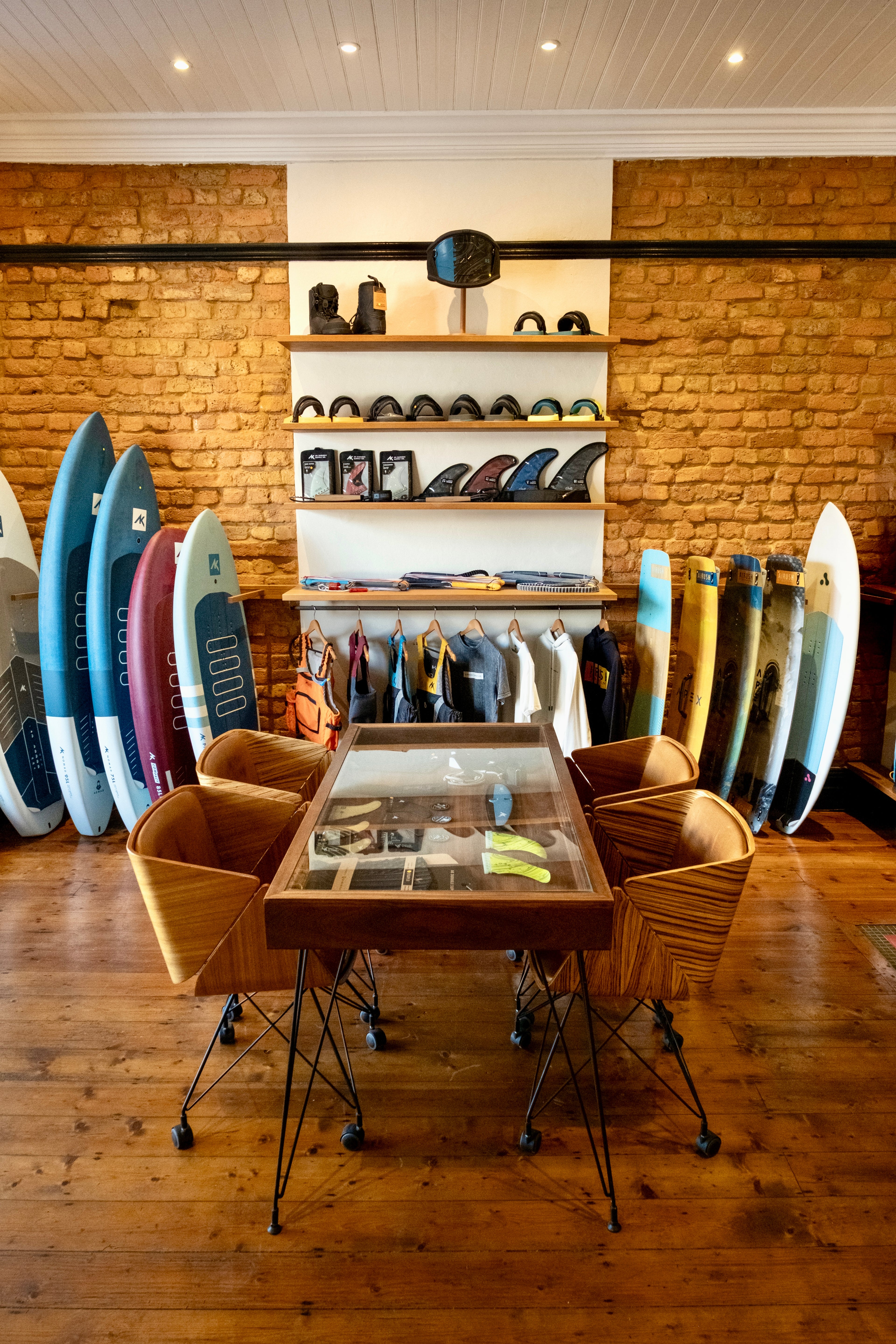 Surfboard shop interior with surfboards, chairs, and a table.
